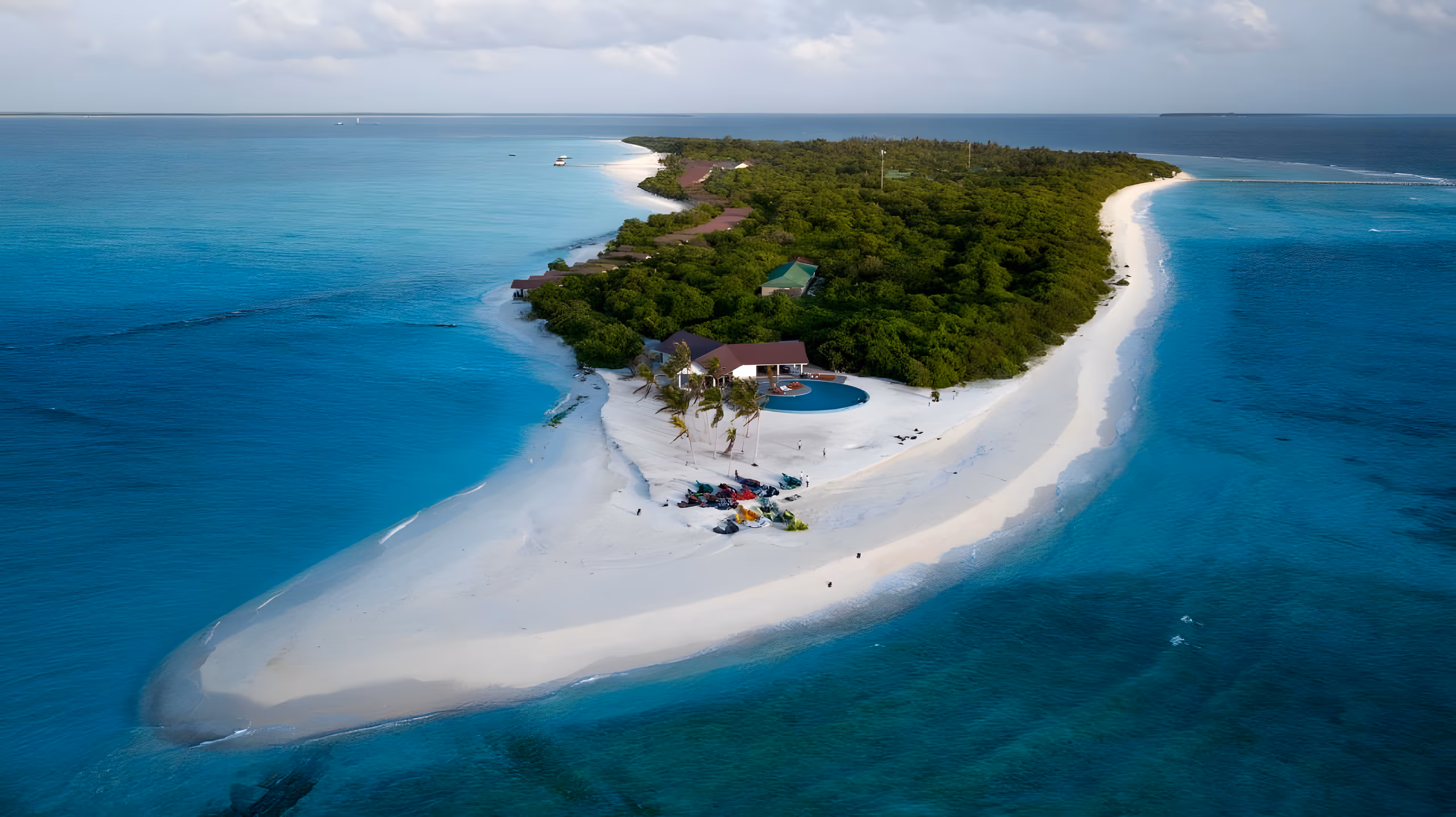 Aerial view of a narrow green island ringed by white sand and turquoise reef water