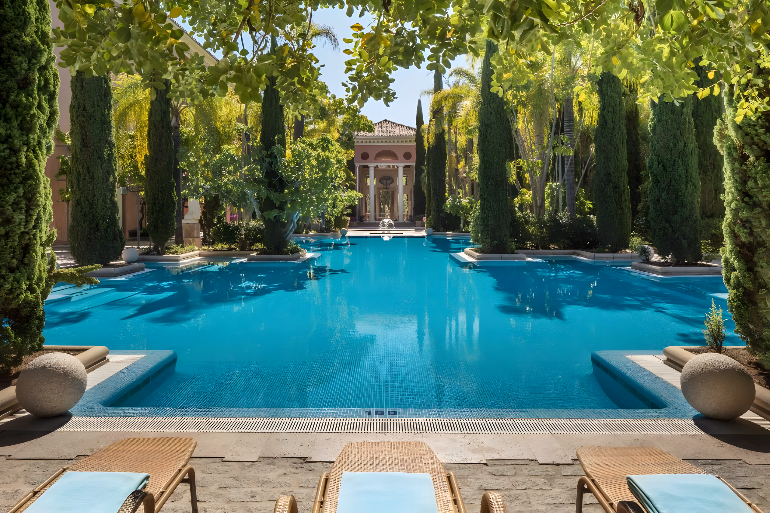 Long turquoise pool flanked by cypress trees leading to a palatial Andalusian facade